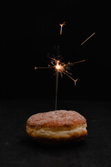 Traditional German or Austrian doughnut typically served for carnival or New Year's Eve filled with rose hip jam and dusted with cinnamon and sugar with sparkler on black background - 523650041