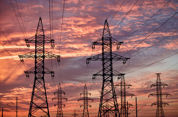 High voltage power lines pylons and electrical cables on a sunset sky background. Modern...