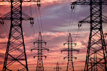 High voltage power lines pylons and electrical cables on a sunset sky background. Modern infrastructure of high voltage transmission lines. Overhead power lines towers equipment. Energy industry.