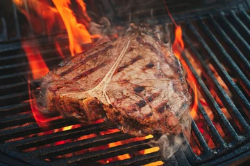 Wandaufkleber Barbecue dry aged wagyu porterhouse beef steak grilled as close-up on a charcoal grill with fire and smoke © HLPhoto