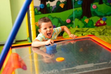 Little child boy playing air hockey and screaming in the play center 
