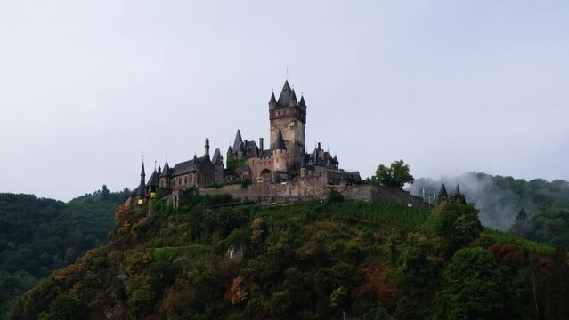 Romantic german medieval hill-top castle among mysterious clouds and rising steam on a rainy summer morning. Reichsburg Cochem is a famous tourist destination in the beautiful Moselle Valley. 4K