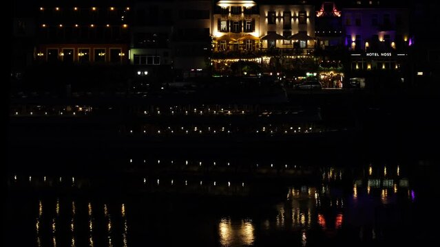 The romantic german medieval town Cochem and the River Moselle by night. Beautiful water reflections, abstract neutral mirror effect, colourful evening lights glittering around. 4K