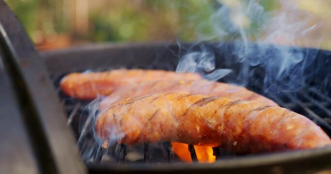 Slow motion video of sausage on BBQ dripping grease and flaming uop