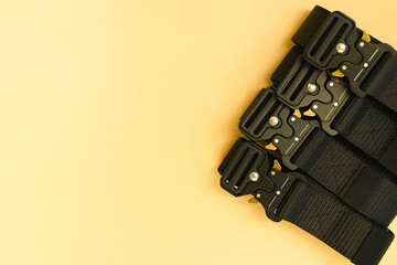 A top view of many black canvas belts with a black fast open metal male buckle and a black belt loop lays on the orange background. Material. Outfit. Safety. Soldier. Steel. Uniform. Weapon. Cloth