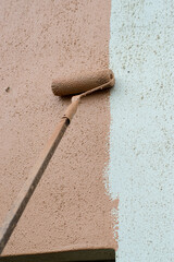 A long paint brush or roller painter of a mason painting and renovating the wall of a architectural...