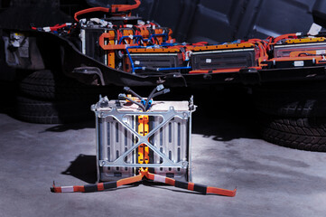 Naklejka premium Electric car lithium power cell with power connections in front of maintained car battery. Blue toned. EV car battery at maintenance.
