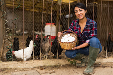 Woman working at a poultry farm is smiling as she holds a basket of newly harvested chicken eggs. © JackF
