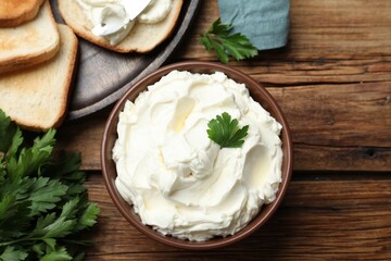 Toasted bread and delicious cream cheese with parsley on wooden table, flat lay