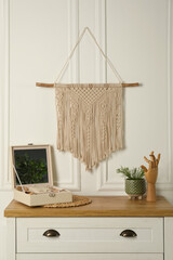 Open jewelry box and decor elements on chest of drawers near white wall with stylish macrame