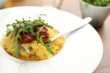 Tasty spaghetti squash with tomato sauce and arugula on table, closeup
