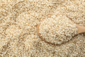 Wooden spoon on pile of white sesame seeds, top view. Space for text