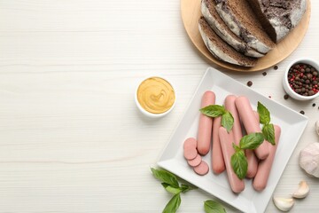 Fresh raw vegetarian sausages with basil, garlic and sauce on white wooden table, flat lay. Space...