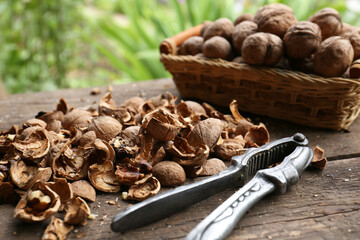 Walnuts, pieces of shells and nutcracker on wooden table against blurred background