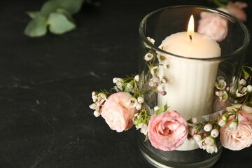Glass holder with burning candle and floral decor on black stone table, closeup. Space for text