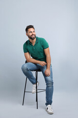 Handsome young man sitting on stool against light grey background