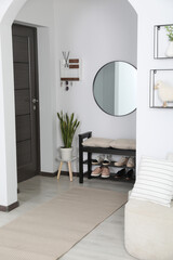 Hallway interior with stylish furniture and round mirror on light wall