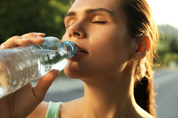 Young woman drinking water outdoors on hot summer day, closeup. Refreshing drink