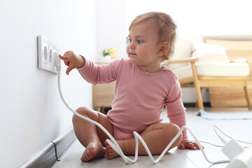 Cute baby playing with electrical socket and plug at home. Dangerous situation
