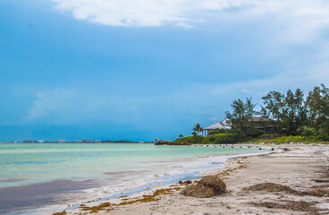 Siesta Key, Florida, popular travel tourist destination. Scene of the beach near Siesta Key Village at dusk as a storm appears in the distant sky. Cool blue turquois water along the rock studded shore