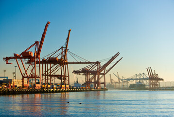 Fototapeta na wymiar Shipping cargo cranes at a port at sunset with blue skies. 