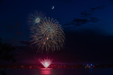 Fireworks celebration with reflections across the river with a town in the background