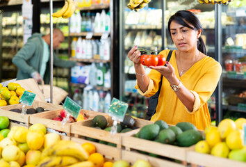 Obraz premium Interested Latina choosing ripe red tomatoes while shopping in vegetable department of grocery store
