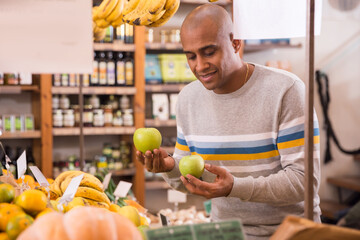 Portrait of smiling Latin American shopper choosing fresh organic apples in grocery store