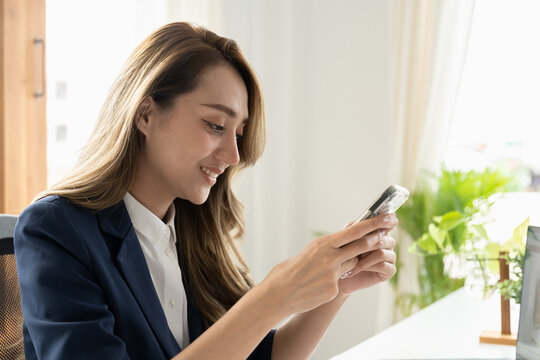 Smiling businesswoman using phone in office. Small business entrepreneur looking at her mobile phone and smiling.