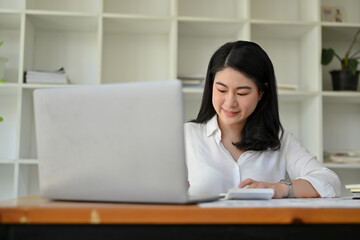 Fototapeta na wymiar Successful Asian businesswoman at her office desk managing her task on laptop.