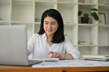 Successful Asian businesswoman at her office desk managing her tasks on her laptop.