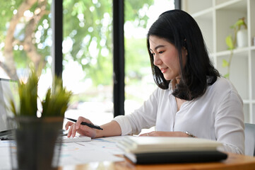 Fototapeta premium Asian female accountant concentrating while working on her sales accounts report