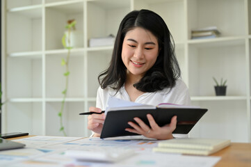 Attractive young Asian female accountant reviewing some detail on her notebook.