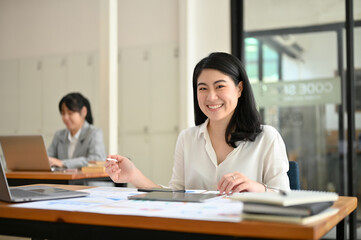 Charming Asian female employee sits at her office desk, working on her financial reports.