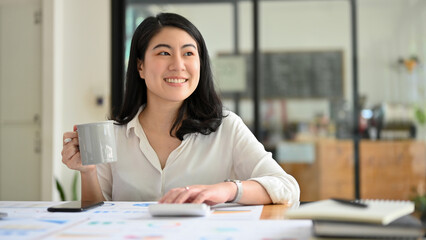 Asian businesswoman at her office desk, daydreaming about success career.