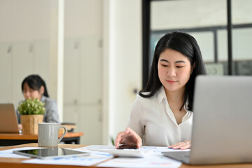 Asian female accountant managing her financial tasks and working at her office desk.