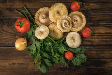 A bunch of fresh dairy wild mushrooms, tomatoes and parsley on a wooden background. Flat lay.