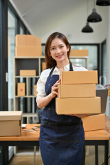 Attractive Asian female e-commerce business startup entrepreneur holding cardboard boxes.