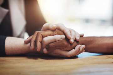 Support, compassion and trust while holding hands and sitting together at a table. Closeup of a loving, caring and interracial couple or friends comforting each other after a loss or cancer news - Powered by Adobe