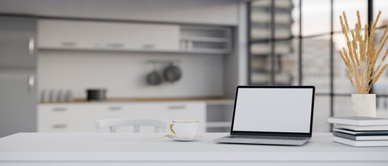 Laptop white screen mockup and copy space on white dining table over blurred kitchen background