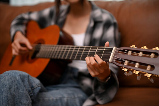A talented female relaxes in her living room and plays her acoustic guitar. cropped image