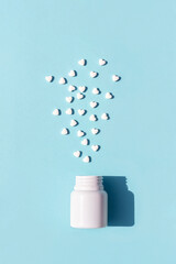 White pills in the shape of heart fly out of bottle on blue background. Medicine, healthcare concept. Top view Flat lay