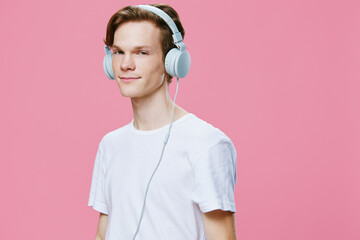 portrait of a handsome, red-haired guy listening to music on headphones while standing on a pink...