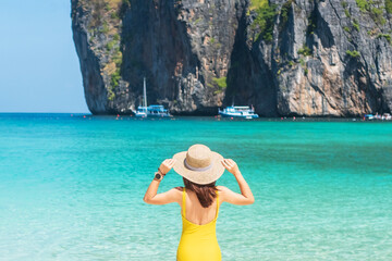 Woman tourist in yellow swimsuit and hat, happy traveller sunbathing at Maya Bay beach on Phi Phi island, Krabi, Thailand. landmark, destination Southeast Asia Travel, vacation and holiday concept