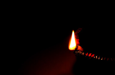 Fototapeta na wymiar Close up image of a lit clay diya or lamp on floor on Diwali - an Indian hindu festival of lights isolated on black background.