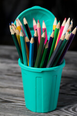 Colored pencils for drawing.  They stand in a pencil holder in the form of a trash can. On pine boards.