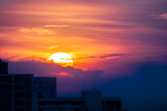 Fototapeta fluffy cloud sky and large round orange sunrise over city for background, image shot with super telephoto lens
