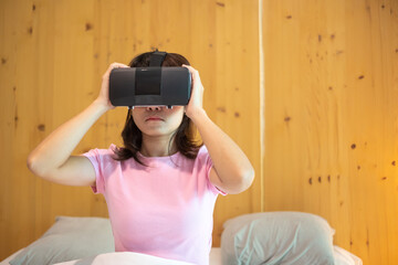 Young woman using virtual reality headset in bed. VR, Future digital technology, game, movies entertainment, metaverse, NFT and 3D cyberspace concept