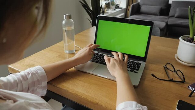 Girl using laptop with green screen in home environment. Slow motion dolly out shot over the shoulder. Perfect for chroma keying.