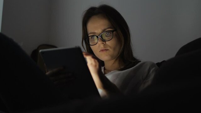 Portrait footage of woman wearing black hipster glasses. She is browsing news or social information feed online on her laptop, smartphone. Monitor screen reflections are in her eyeglasses glass.